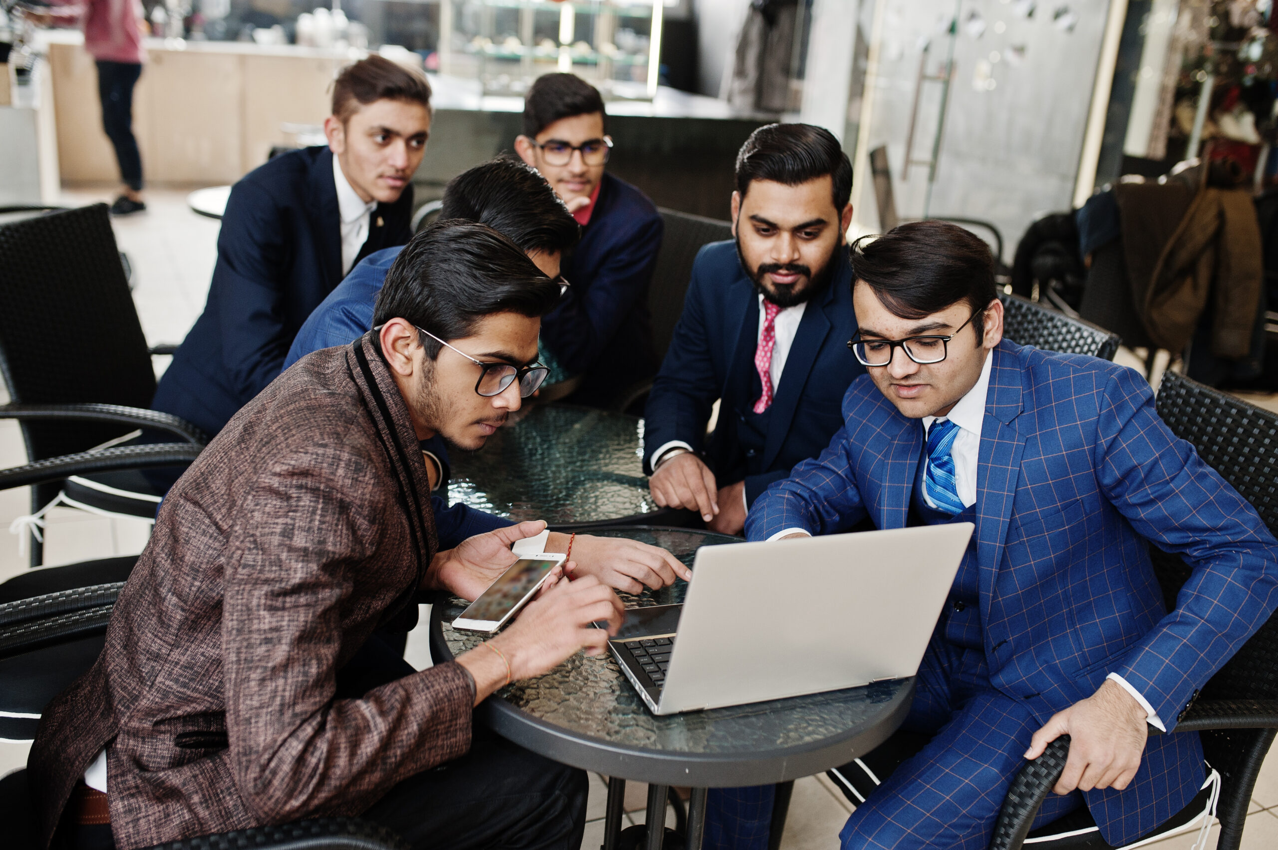Group of six indian business man in suits sitting at office on cafe and looking at laptop.